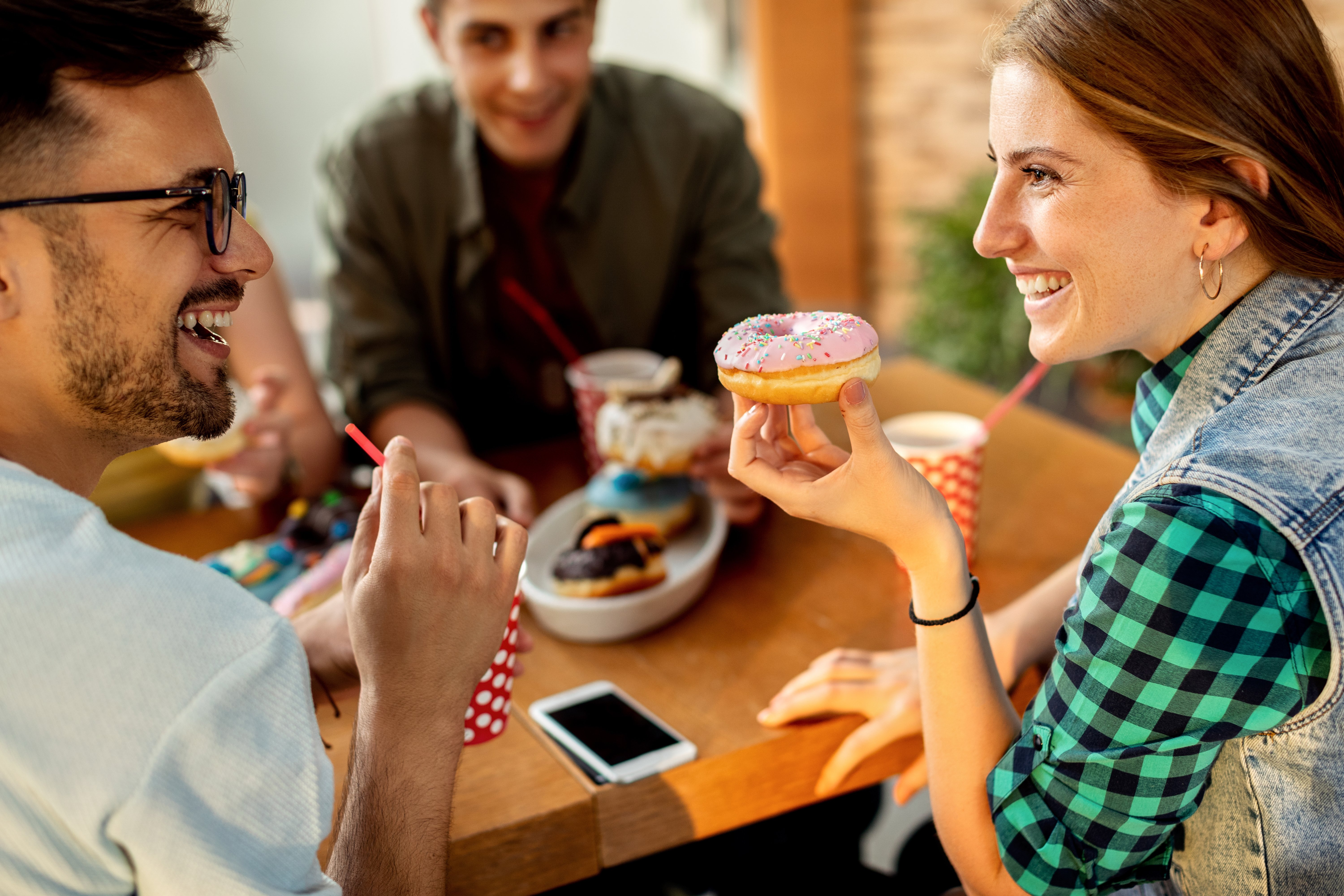 happy-couple-talking-while-eating-donuts-with-friends-cafe